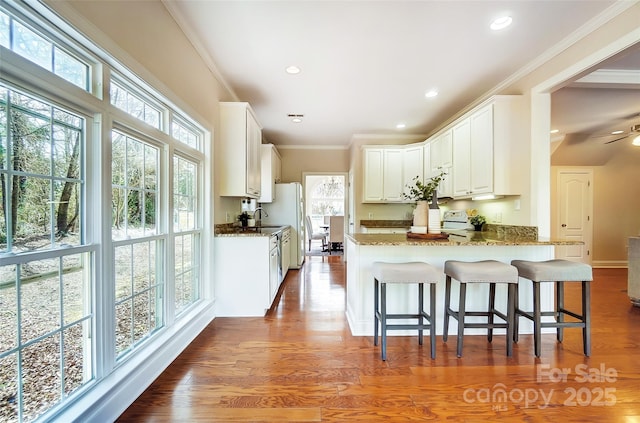 kitchen with dark wood finished floors, dark stone countertops, a peninsula, crown molding, and a sink