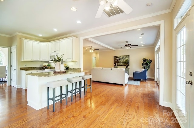 kitchen featuring a breakfast bar, crown molding, light wood finished floors, white microwave, and white cabinetry