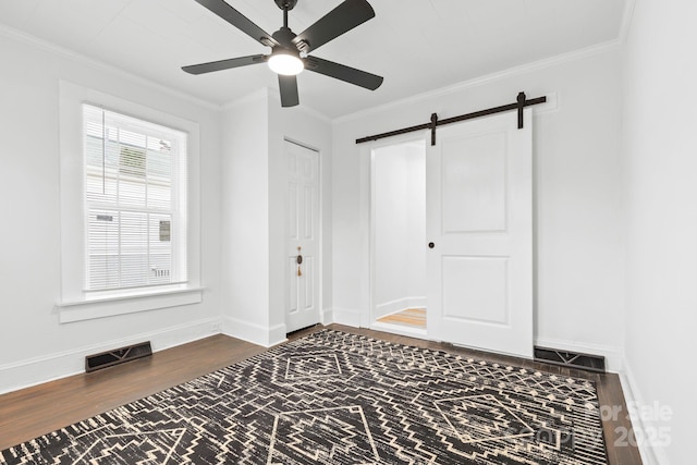 unfurnished room with visible vents, ornamental molding, a barn door, and wood finished floors