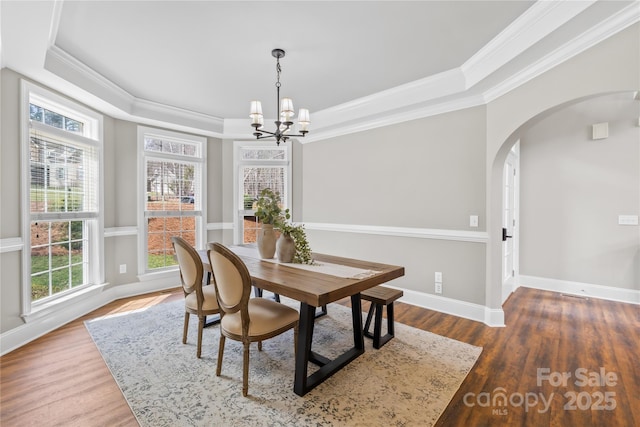 dining room with a tray ceiling, wood finished floors, arched walkways, and ornamental molding