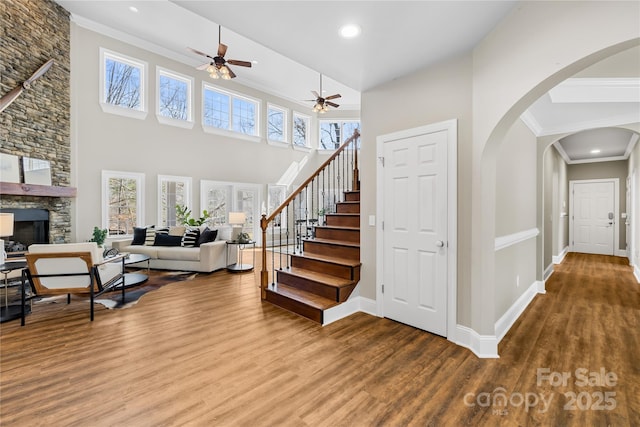 staircase with wood finished floors, baseboards, a fireplace, arched walkways, and crown molding