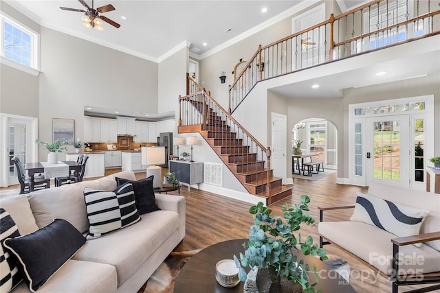 living area featuring arched walkways, stairway, light wood-style floors, and ornamental molding