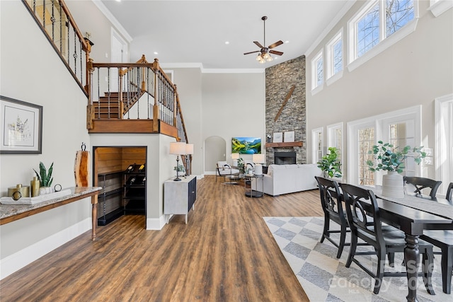 dining room featuring wood finished floors, baseboards, arched walkways, ornamental molding, and a stone fireplace