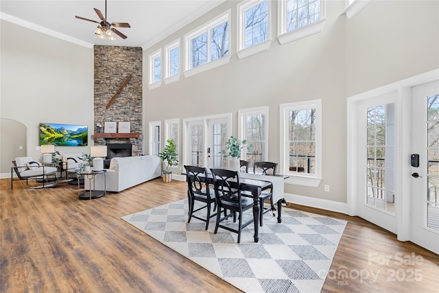 dining area with a stone fireplace, crown molding, baseboards, and wood finished floors