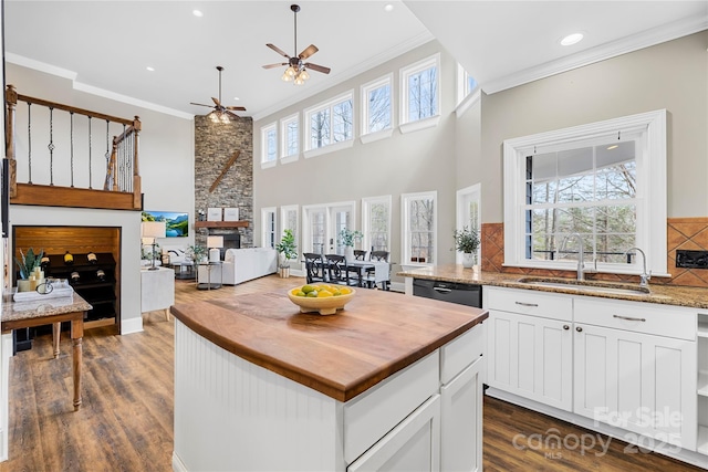 kitchen with a sink, a stone fireplace, butcher block counters, and crown molding