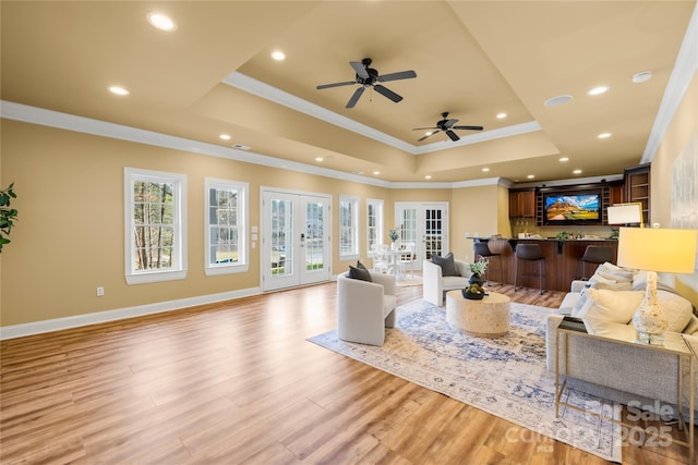 living room with baseboards, a tray ceiling, ornamental molding, french doors, and light wood-type flooring