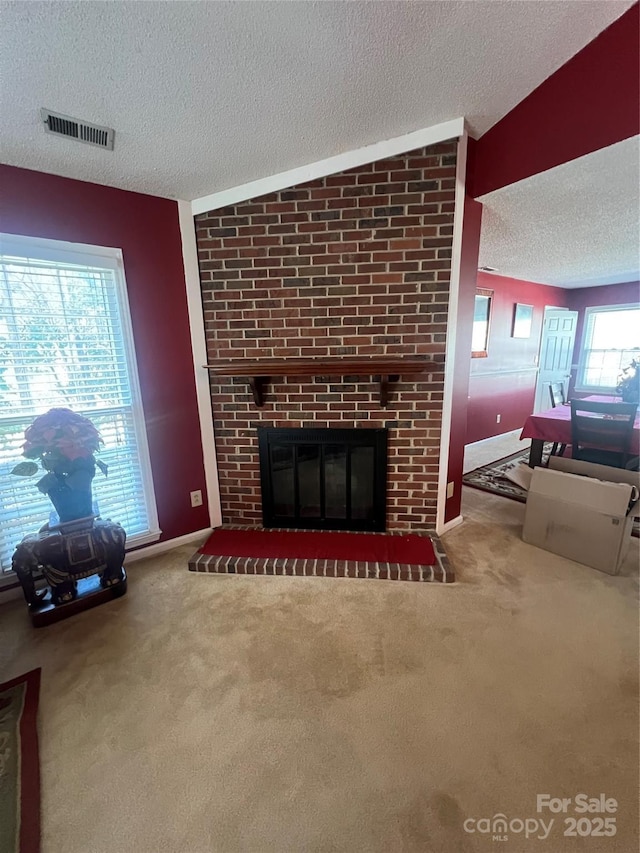 unfurnished living room with a textured ceiling, carpet, a fireplace, and visible vents