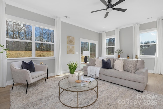 living area featuring wood finished floors, a ceiling fan, visible vents, baseboards, and ornamental molding