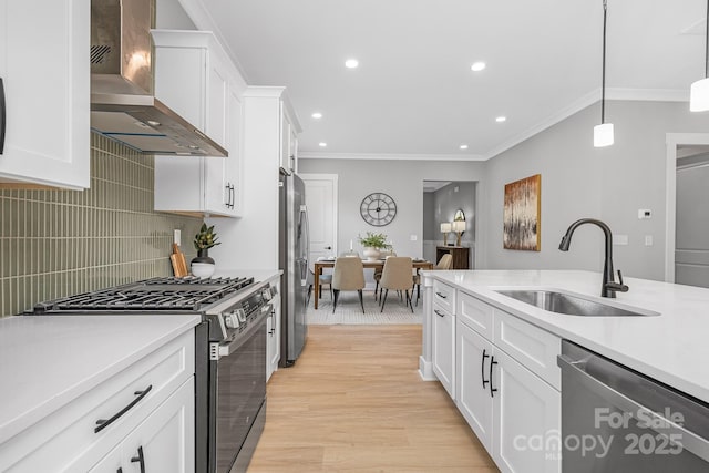 kitchen with light countertops, appliances with stainless steel finishes, ornamental molding, a sink, and wall chimney exhaust hood