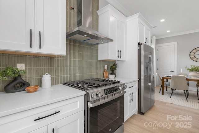 kitchen featuring stainless steel appliances, white cabinets, wall chimney range hood, tasteful backsplash, and crown molding