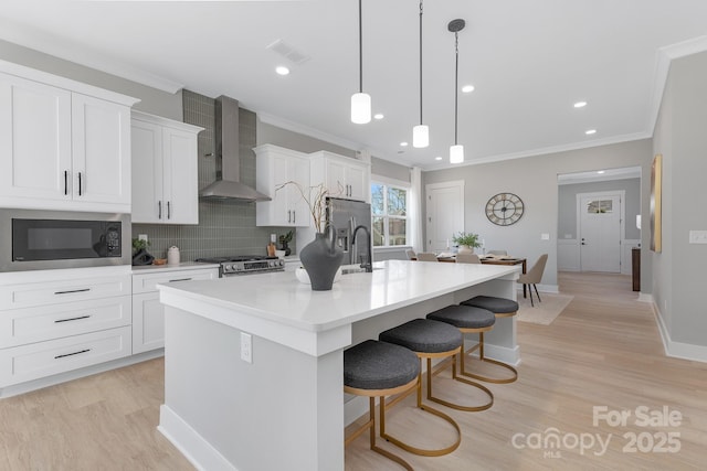 kitchen featuring visible vents, stove, a kitchen island with sink, built in microwave, and wall chimney exhaust hood