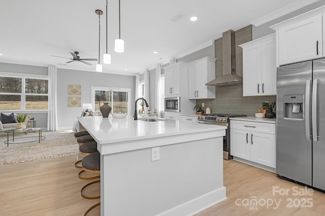 kitchen featuring wall chimney range hood, light wood-style flooring, stainless steel appliances, and a sink