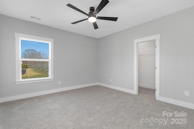 unfurnished bedroom featuring a walk in closet, light colored carpet, visible vents, a ceiling fan, and baseboards