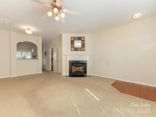 unfurnished living room featuring baseboards, carpet, a tiled fireplace, arched walkways, and a ceiling fan