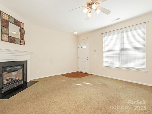 unfurnished living room with visible vents, a fireplace with flush hearth, carpet flooring, baseboards, and ceiling fan