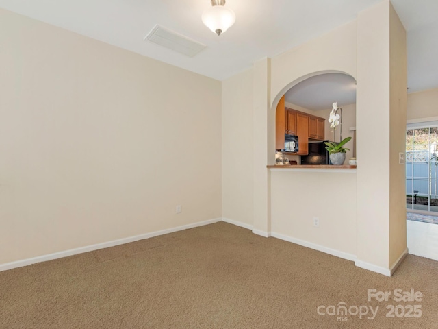 carpeted spare room featuring visible vents, baseboards, and arched walkways