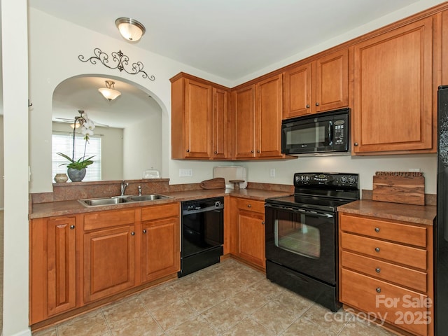 kitchen featuring brown cabinetry, arched walkways, a sink, black appliances, and dark countertops