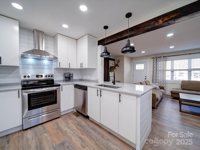 kitchen with stainless steel appliances, open floor plan, hanging light fixtures, light countertops, and wall chimney exhaust hood