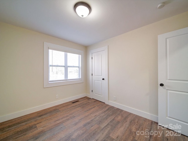 unfurnished room featuring dark wood-type flooring, visible vents, and baseboards