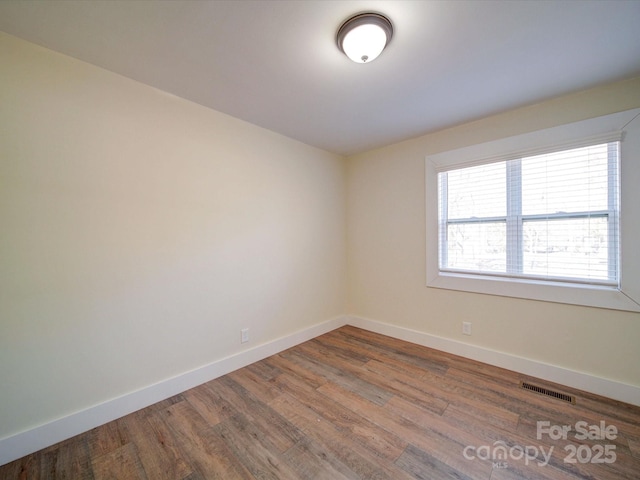 spare room with wood finished floors, visible vents, and baseboards