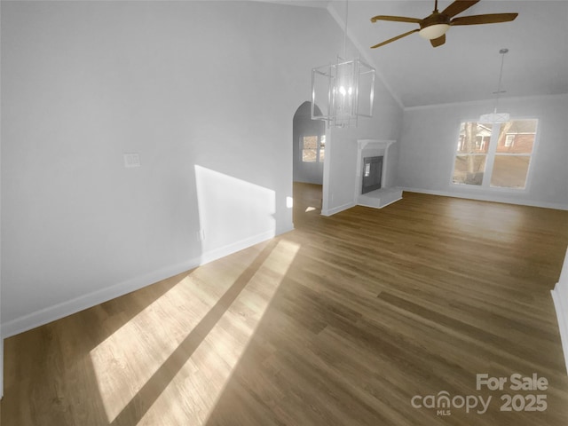 unfurnished living room featuring arched walkways, a glass covered fireplace, ceiling fan, wood finished floors, and high vaulted ceiling