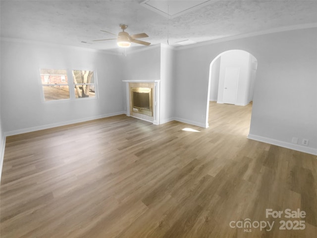 unfurnished living room featuring a textured ceiling, a fireplace, wood finished floors, baseboards, and attic access