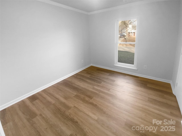 empty room with ornamental molding, wood finished floors, and baseboards