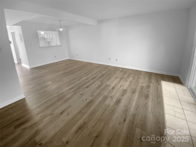 empty room featuring ceiling fan, wood finished floors, beam ceiling, and baseboards