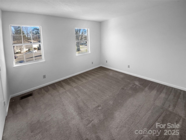 unfurnished room with dark colored carpet, visible vents, and baseboards