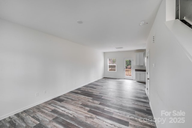 unfurnished living room with baseboards and dark wood-type flooring