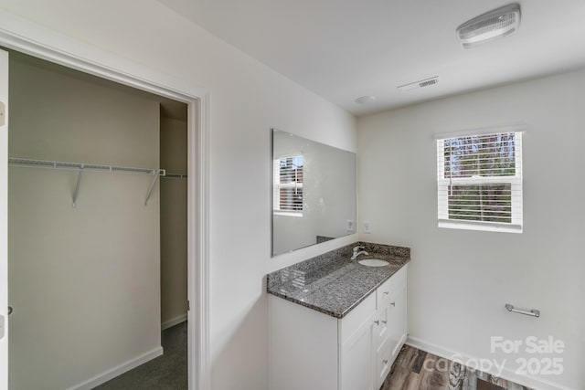bathroom with a walk in closet, vanity, visible vents, and baseboards