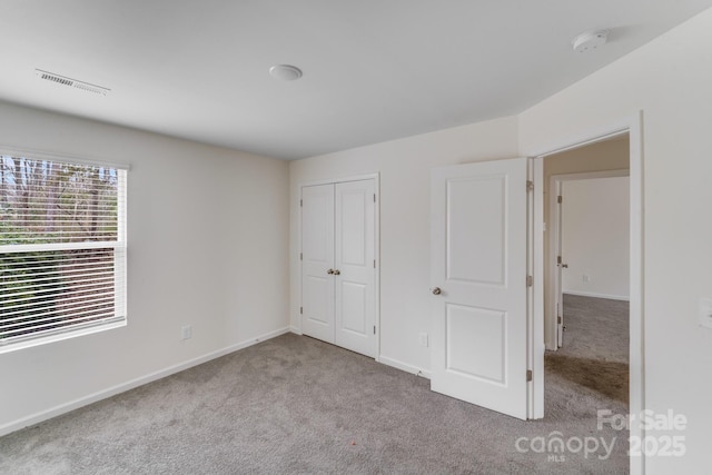 unfurnished bedroom with a closet, light colored carpet, visible vents, and baseboards