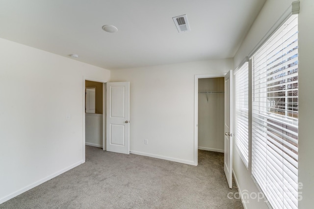 unfurnished bedroom with visible vents, baseboards, light colored carpet, a spacious closet, and a closet