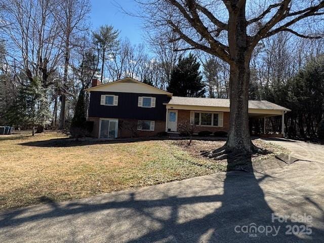 split level home with a chimney, a front lawn, an attached carport, and concrete driveway