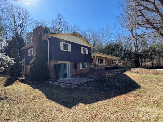 rear view of house featuring brick siding, a yard, and a chimney