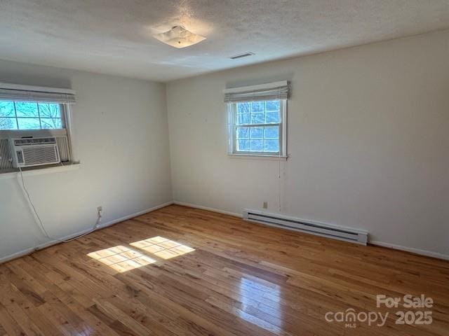 spare room with baseboard heating, wood-type flooring, cooling unit, and visible vents