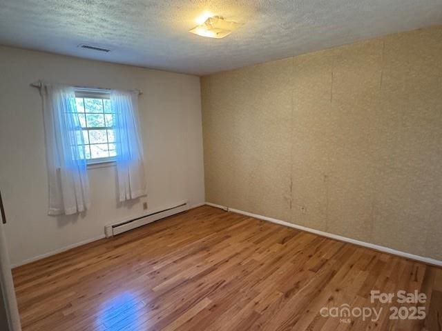 unfurnished room with a textured ceiling, baseboard heating, wood finished floors, and visible vents