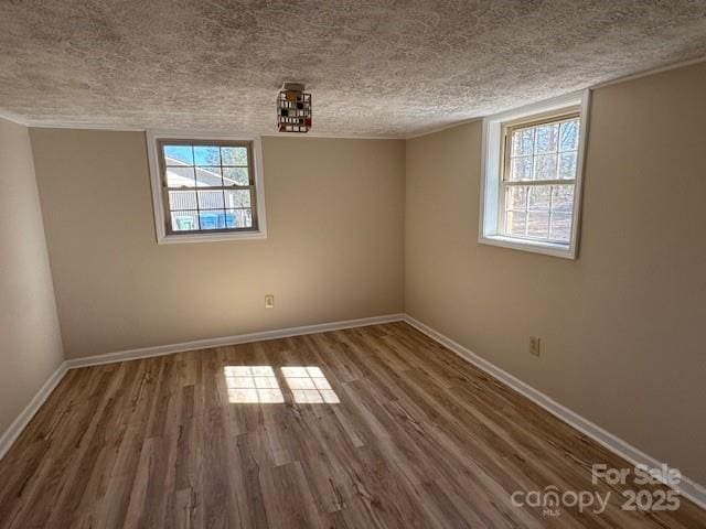 empty room featuring a textured ceiling, dark wood finished floors, and baseboards