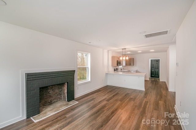 unfurnished living room featuring dark wood finished floors, visible vents, an inviting chandelier, a brick fireplace, and baseboards