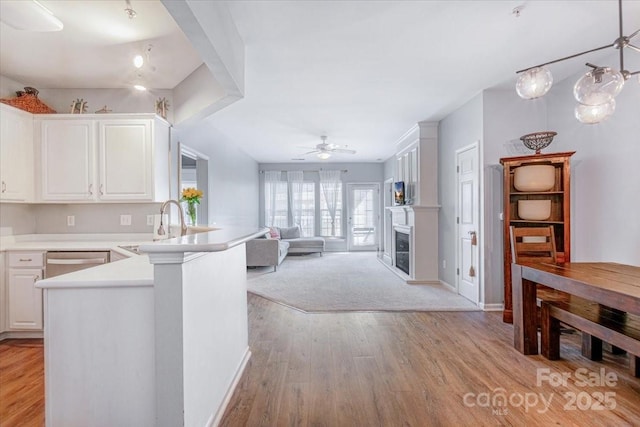 kitchen featuring a peninsula, a fireplace, white cabinetry, stainless steel dishwasher, and light wood finished floors