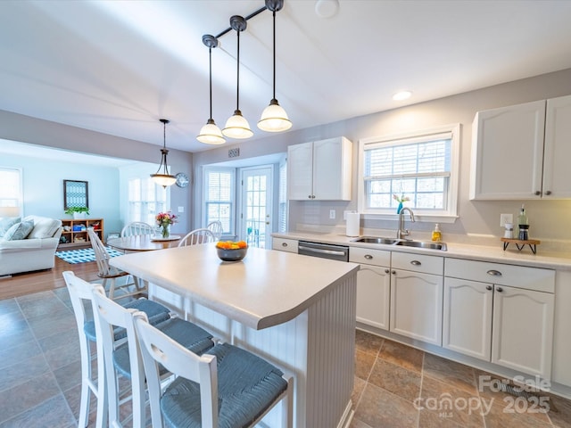 kitchen with decorative light fixtures, light countertops, open floor plan, white cabinets, and a sink