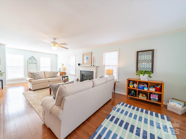 living area with ceiling fan, ornamental molding, wood finished floors, and a glass covered fireplace