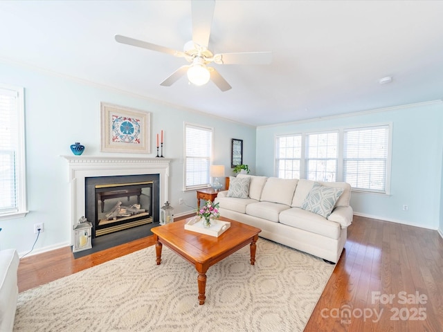 living room with ornamental molding, a fireplace with flush hearth, ceiling fan, wood finished floors, and baseboards