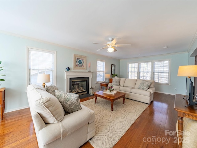 living room with baseboards, wood finished floors, a fireplace with flush hearth, and crown molding