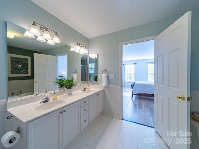 ensuite bathroom with ensuite bathroom, double vanity, wainscoting, and a sink