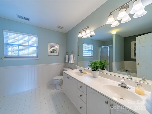 bathroom with a wainscoted wall, a sink, visible vents, a bath, and a stall shower