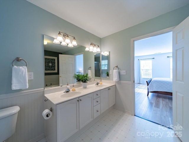 full bath with double vanity, a wainscoted wall, a sink, and ensuite bathroom