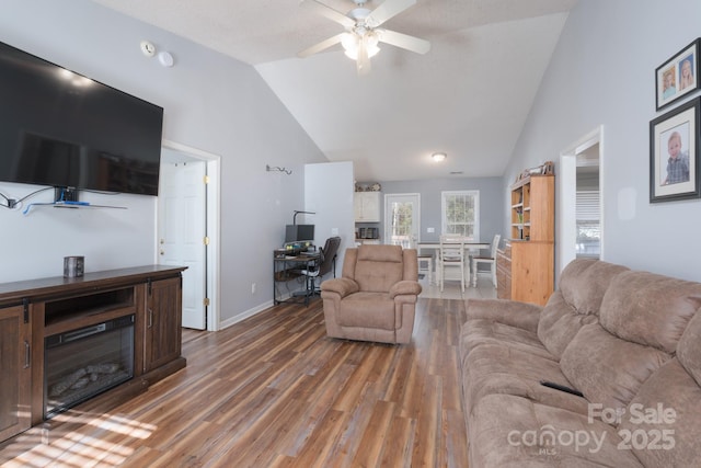 living room featuring a ceiling fan, high vaulted ceiling, baseboards, and wood finished floors