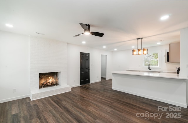 kitchen with dark wood finished floors, open floor plan, a peninsula, light countertops, and a fireplace