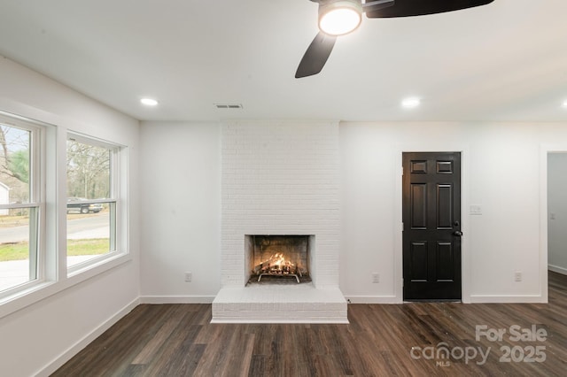 unfurnished living room featuring dark wood-style flooring, a brick fireplace, visible vents, and baseboards